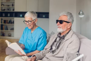 Picture of medical caregiver reading to patient who is visually impaired wearing dark glasses