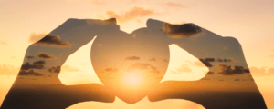 A transparent shadow of hands holding a heart with a sunset horizon background.